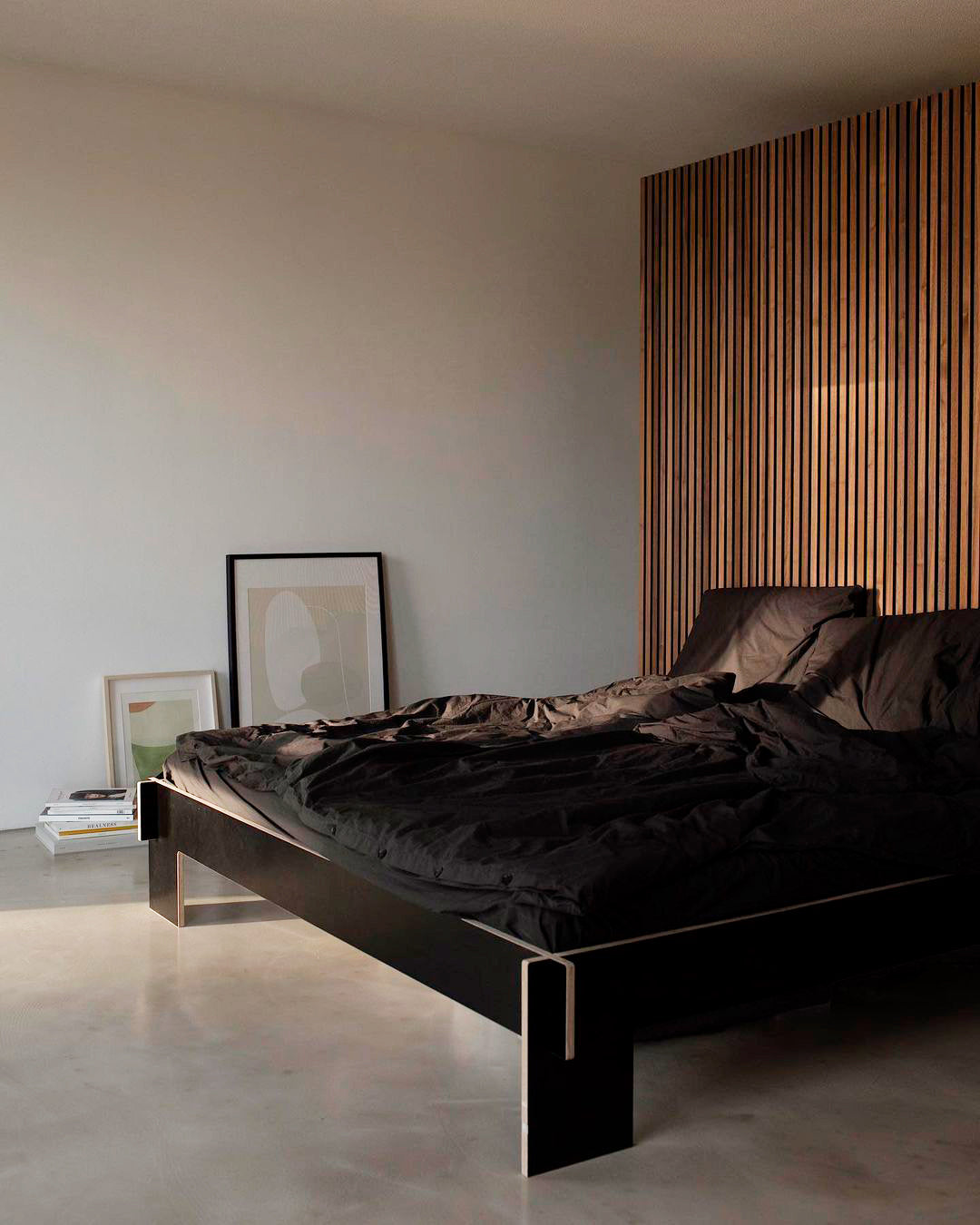 minimalist bedroom with dark bedding, oversized art frames and a vertical wood slat wall behind the bed
