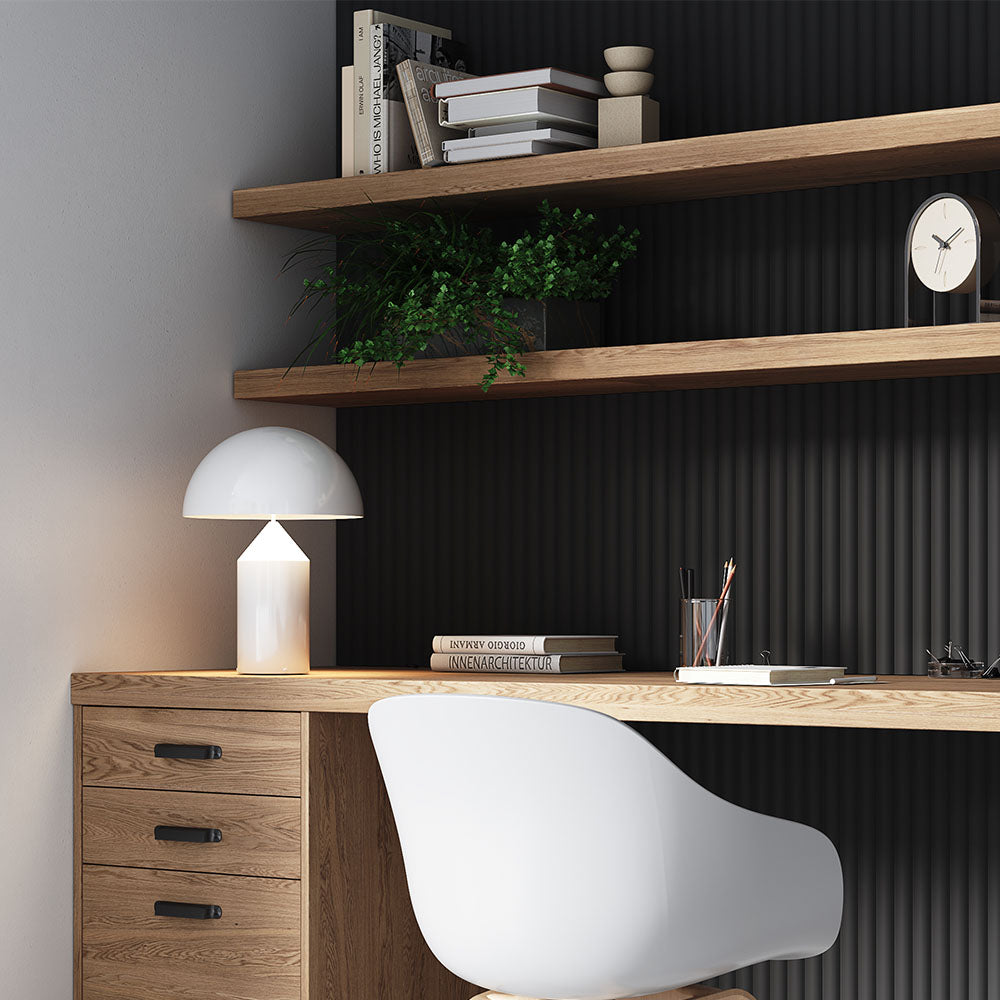 A minimalist home office featuring a black slat accent wall, wooden floating shelves, and a light wood desk. The space is organized with books, a modern white desk chair, and a small potted plant for a touch of greenery.