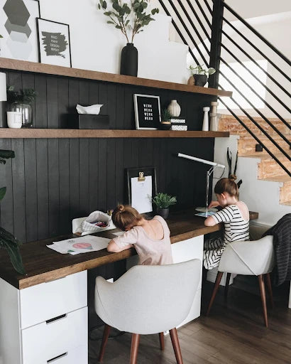 two kids doing homework in a home office with an accent wall