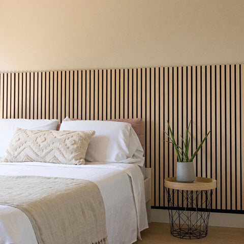 A cozy bedroom featuring a bed with white linens and a decorative headboard made of wooden acoustic wall panels, highlighting the importance of knowing how to clean acoustic wall panels.