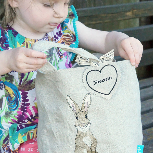 Little girl looking inside an embroidered rabbit Easter egg hunting bag by Kate Sproston Design