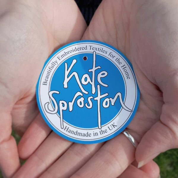 Two hands holding a Kate Sproston Design swing tag