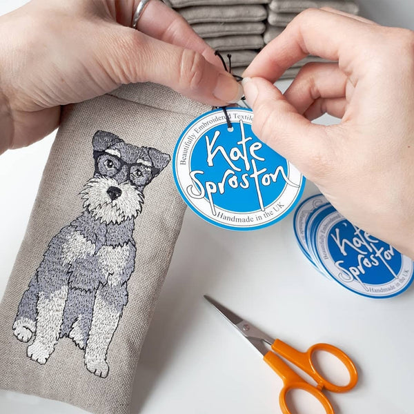 Hands tying a swing tag to an embroidered schnauzer glasses case by Kate Sproston Design