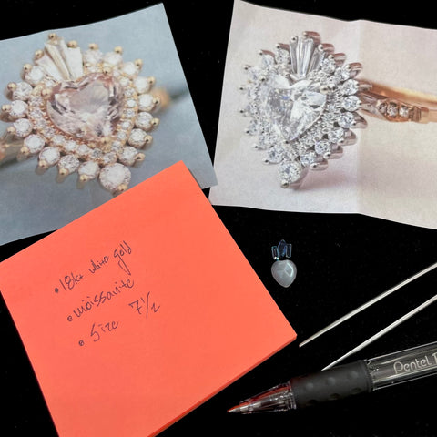 Beginning of custom jewelry design process.  One loose moonstone is shown beneath two sapphires and an aquamarine, a grouping surrounded with two photos of ring designs and a notepad with notes personalized to the order.