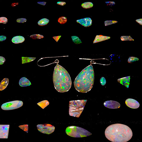 Two fine Mexican crystal opals bezel set into 14 karat white gold dangle earrings surrounded by a rainbow of different loose opal cabochons.