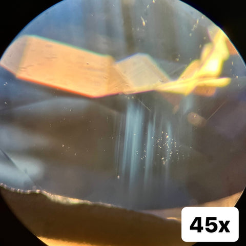 A natural blue sapphire under 45x magnification, focusing on straight rutile inclusions that are cloudy from heat treatment.