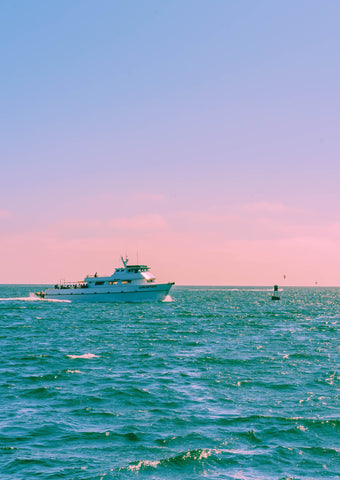 Yacht at sea as the sun sets in the distance. The colors are bright yet hazy with a nostalgic feel.