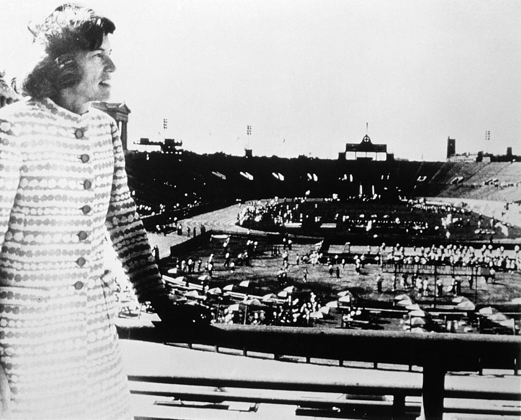 Special Olympics Gründerin Eunice Kennedy Shriver steht auf der Tribüne in einem Stadion. Im Hintergrund sind Athleten zu sehen.
