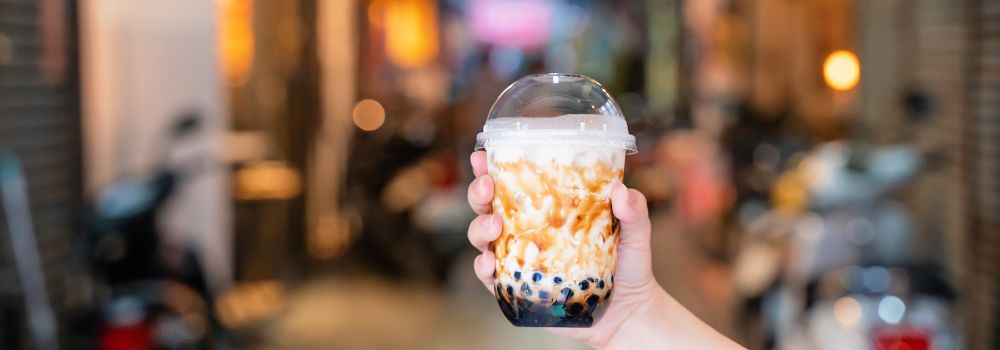 Hand holding brown sugar milk tea with boba in front of well-lit street