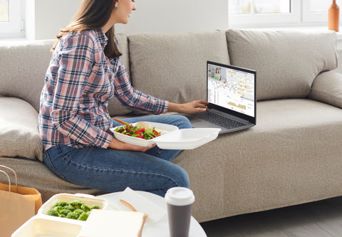 Women eating take out on the couch in front of her laptop