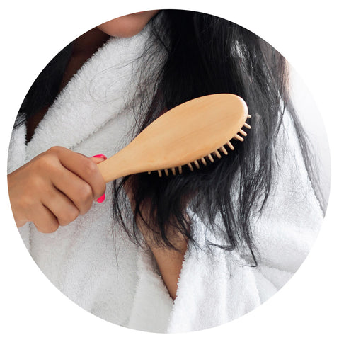 woman detangling the ends of her hair with a brown detangling brush