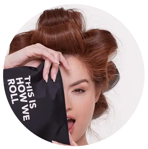 woman with red hair in rollers holding up a black bag with white lettering