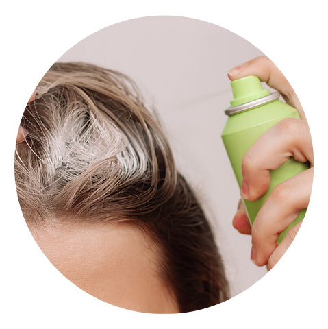 close-up of a woman spritzing dry shampoo onto her hair