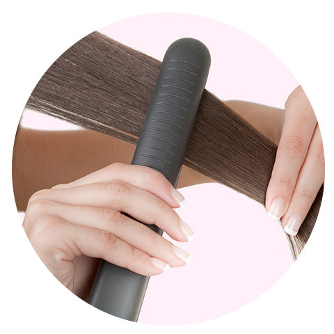 woman with brown hair straightening her hair with a flat iron