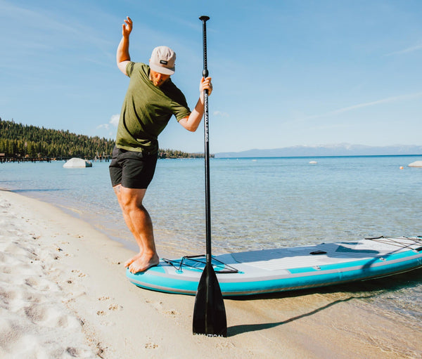 Man making funny pose as he stands on the bow of a NAUTICAL standup paddleboard on the beach shoreline