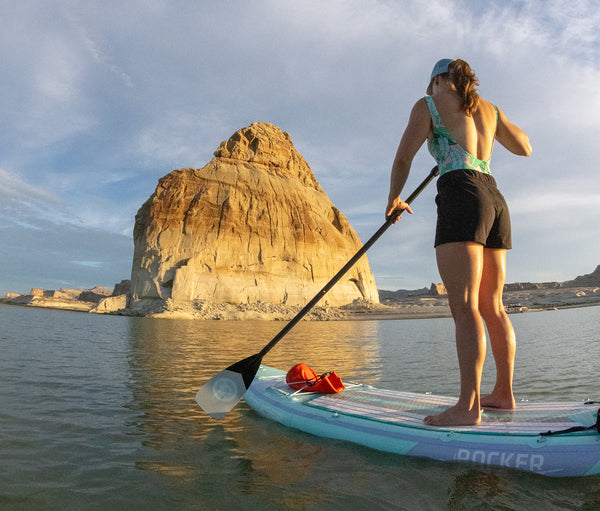 Woman paddling on a iROCKER standup paddle board on rocky shoreline