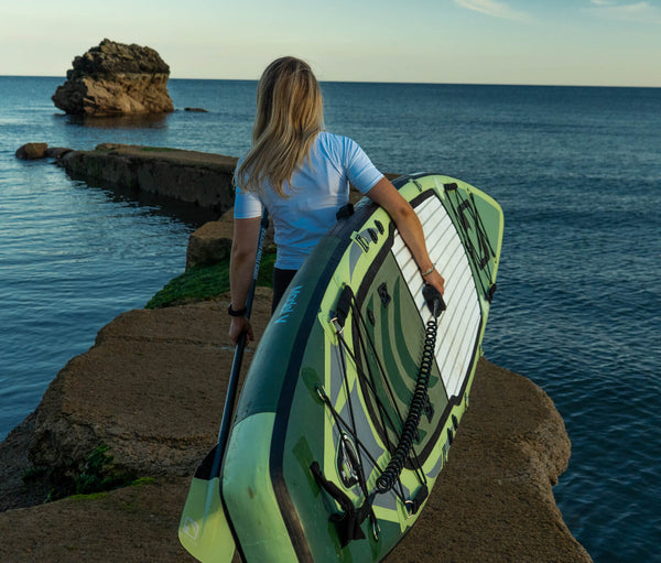 Woman carrying BLACKFIN standup paddle board on rocky shoreline