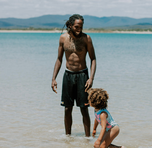 Black man wears running shorts while swimming in ocean with daughter