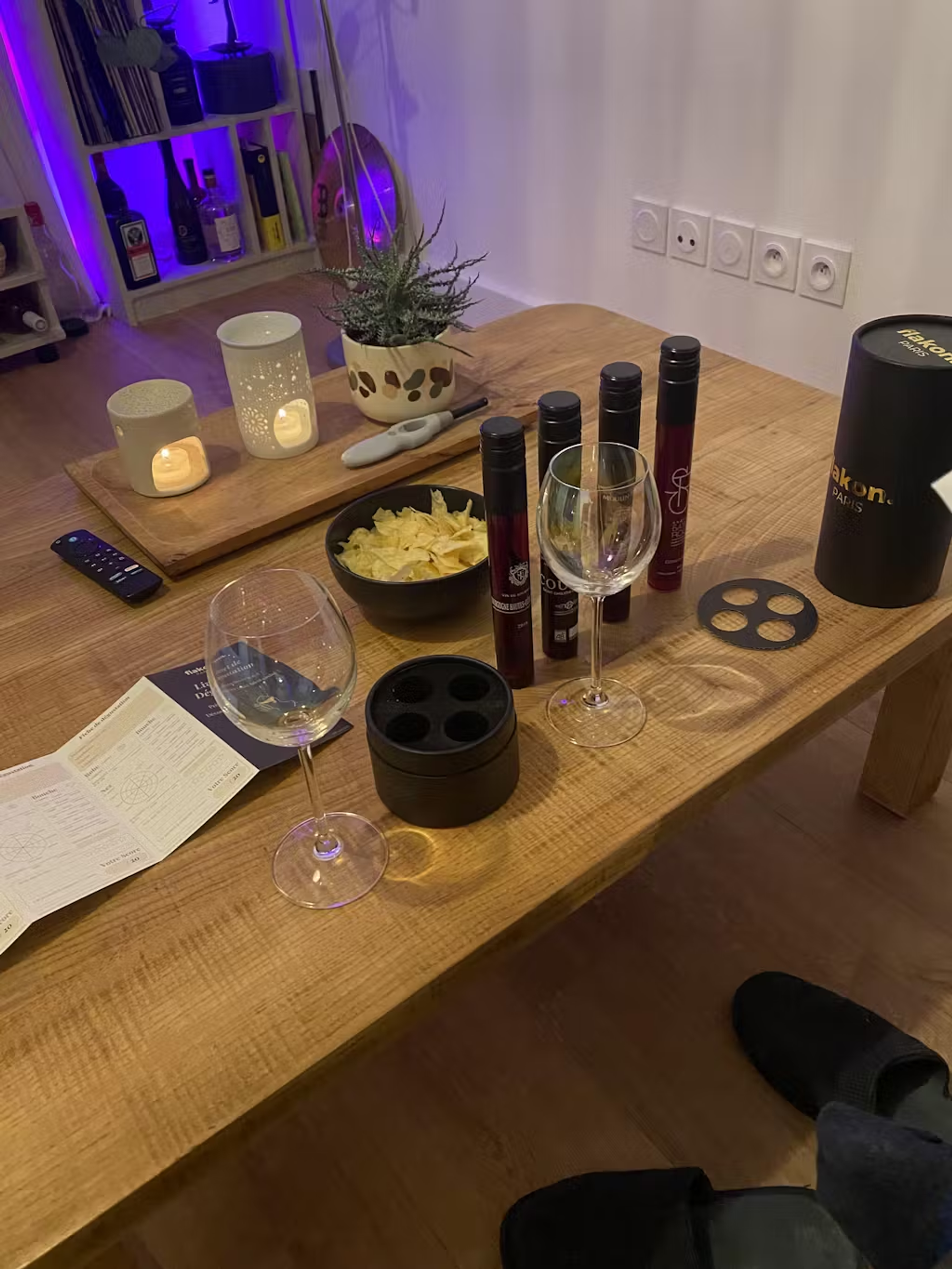 Cozy indoor setting with snacks, wine tasting set, candles, and smart speaker on a wooden table.