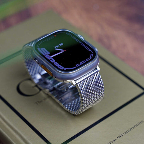 Stainless steel Milanese Apple Watch strap by Buckle and Band, being displayed on top of a book on a table