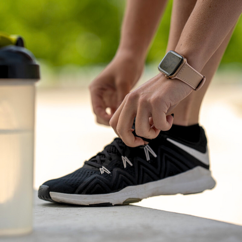 Mona Pink Apple Watch workout strap, being worn by a woman adjusting her trainers whilst on a run. With a water bottle in the foreground
