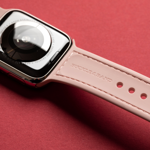 Pink Mona Apple Watch sports strap by Buckle and Band laid out on a red surface