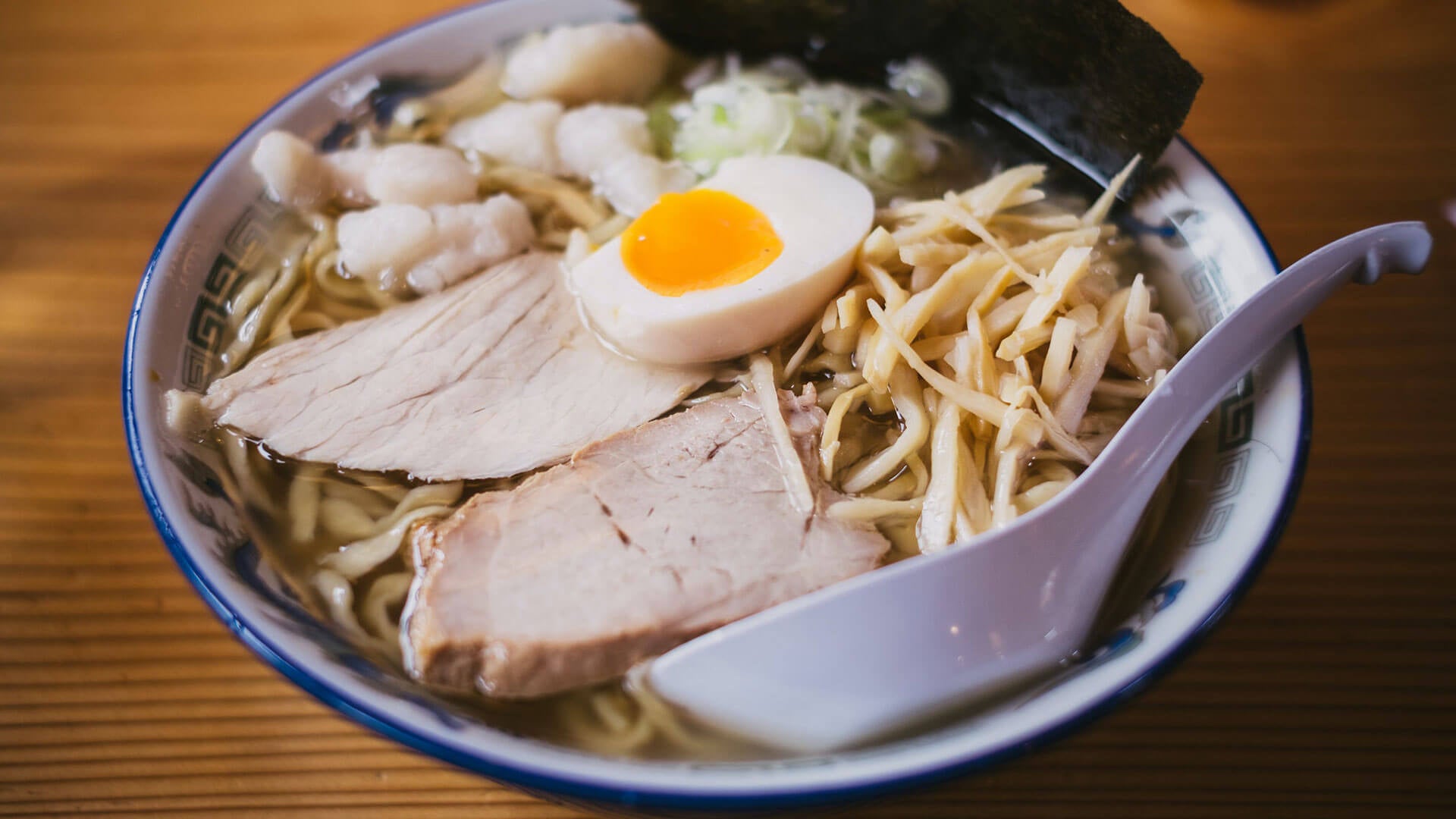 Bowl of ramen with pork, egg, and spoon.