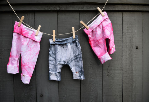 Three pairs of KOOSHOO Kids Pants hang on a clothesline, two pairs of pink Batik and one pair of black Batik in the middle.
