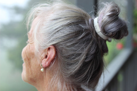 A grey-haired model wears her hair up in small bun using a KOOSHOO plastic-free, organic hair tie.