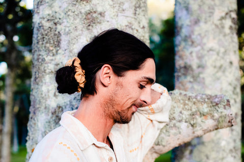 A male model secures his hair into a low man bun using a KOOSHOO plastic-free, organic cotton scrunchie.