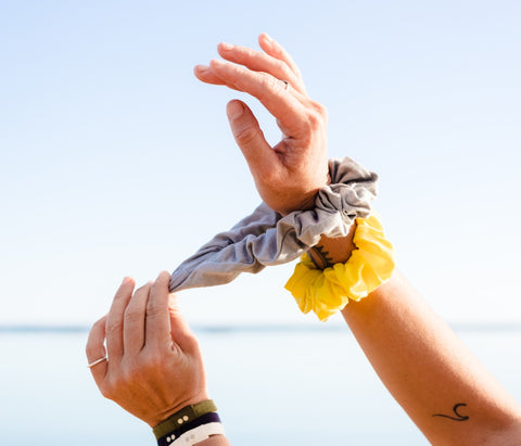 A model's arms against an ocean backdrop with her right arm containing KOOSHOO organic cotton scrunchies.