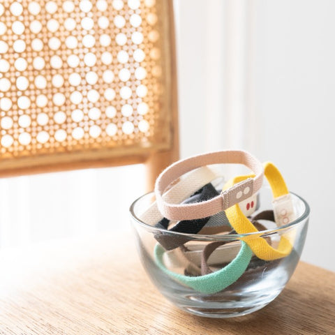 A clear bowl of kooshoo plastic-free hair ties sits on a light brown chair in the sunlight.