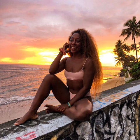 Woman sitting on rock wall in hawaii with coral rose scrunchie on her wrist