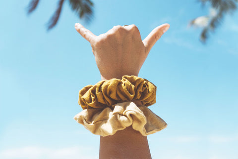 KOOSHOO organic scrunchies on a person's left arm making the "shaka" symbol with their fingers