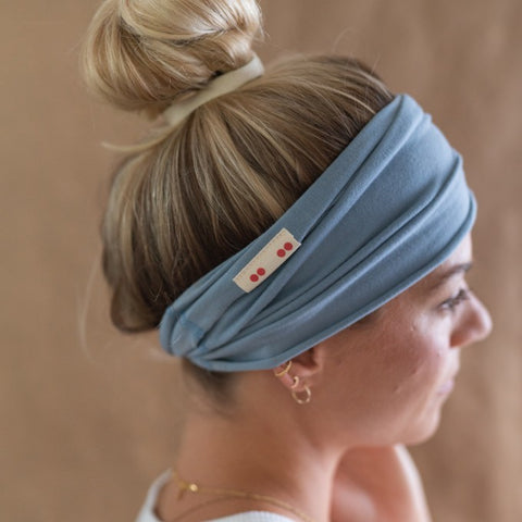 A profile photo of Katrin wearing a blue Kooshoo headband with her blonde hair in a top knot bun.