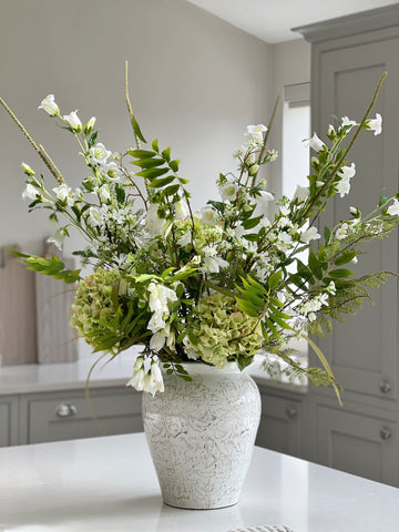 Green and white faux flower arrangement in ceramic vase