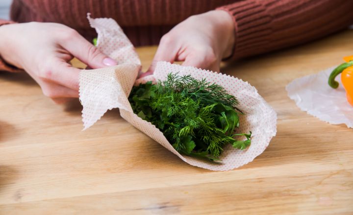a woman wrapping herb inside a beeswax wrap on a wooden table