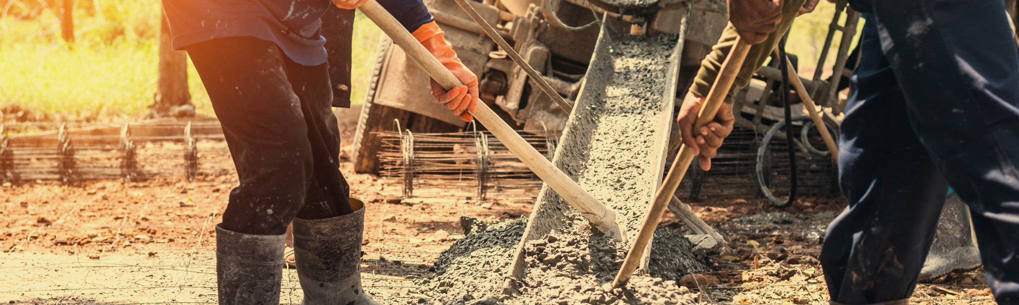 Zwei Bauarbeiter verarbeiten Zement, der aus einem LKW-Zementmischer herausläuft