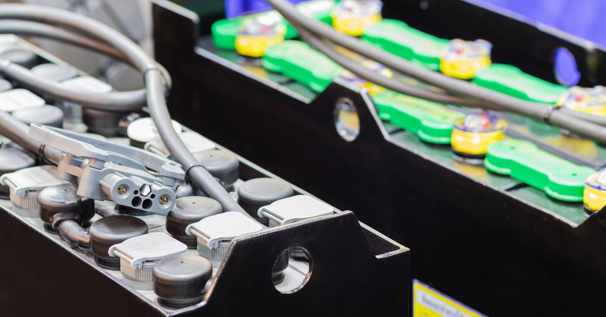 Two industrial automotive batteries sitting next to one another with connective cables attached to the tops of them.