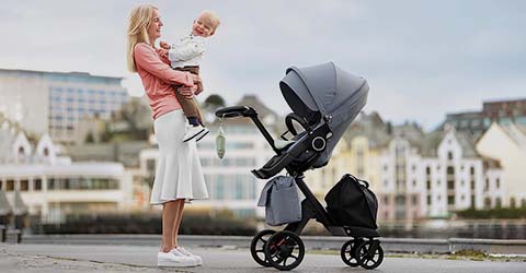 Mother holding her baby while a travel system is nearby