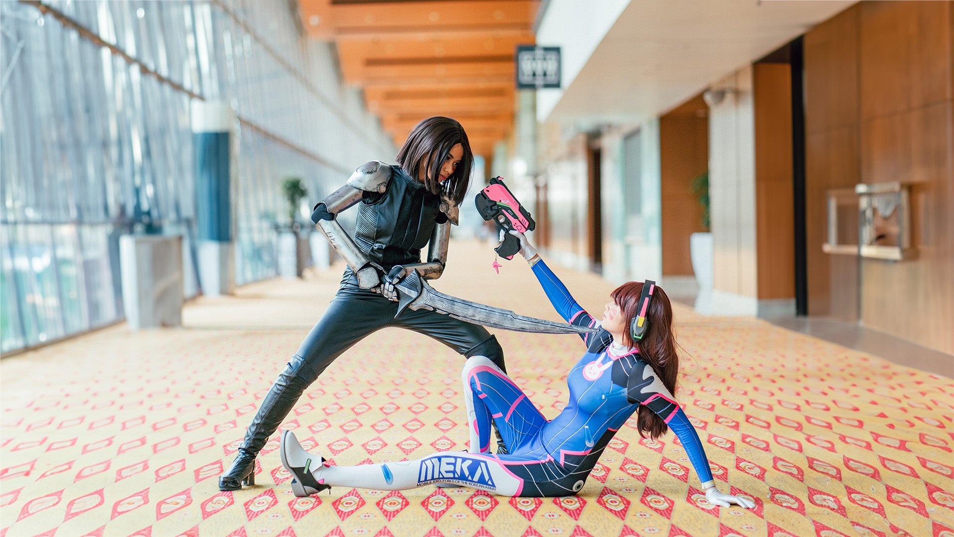 Zwei Frauen, die Charaktere aus Videospielen Cosplayen, kämpfen miteinander. Eine Frau liegt auf dem Boden und richtet ihre Waffe auf die stehende Frau.