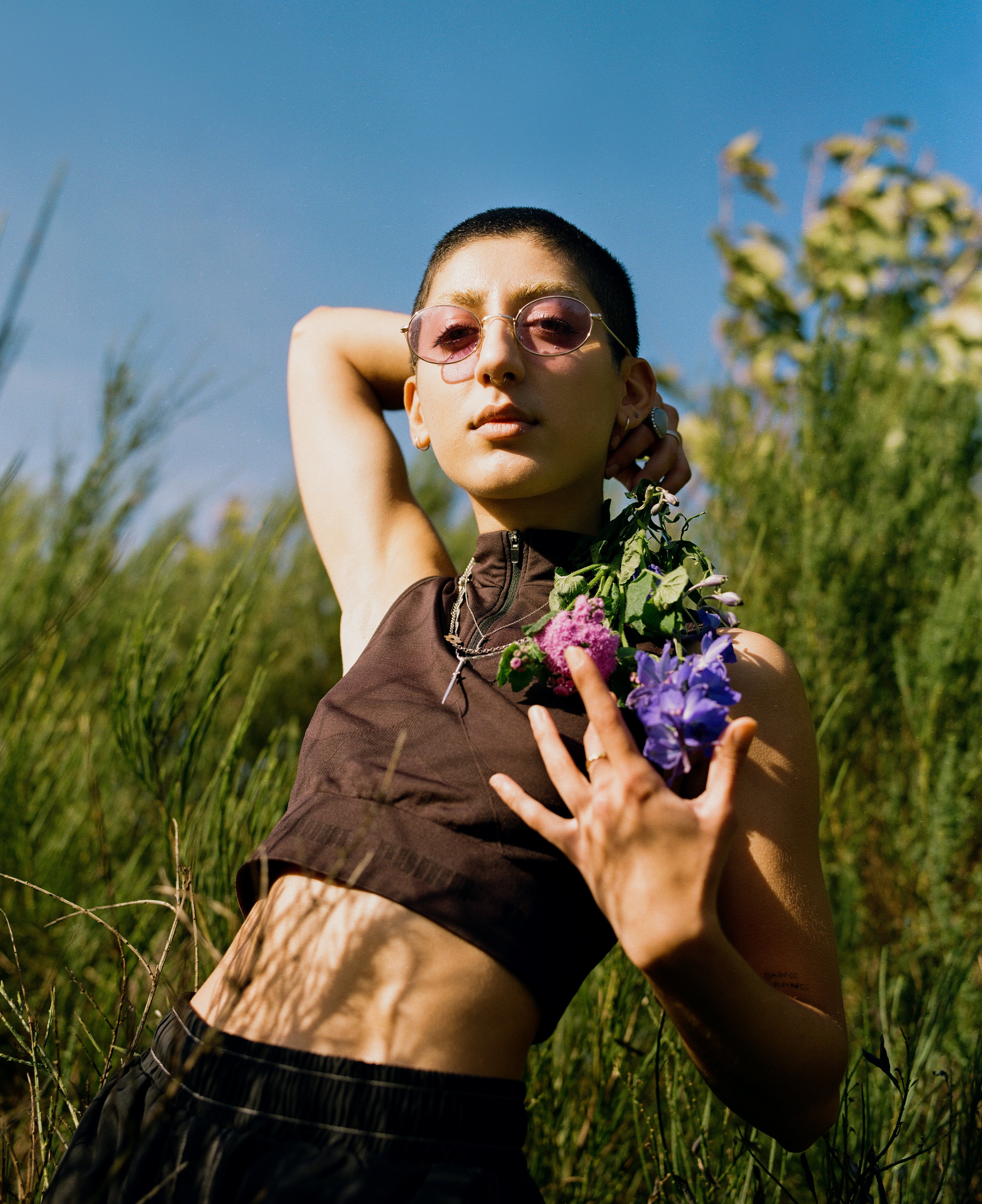 Model wearing sunglasses poses with purple flowers