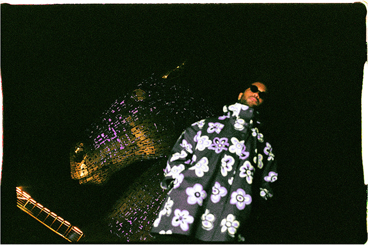 Film photograph of musician Billy Got Waves in hooded jacket in front of illuminated horse sculpture at night by Craig McIntosh