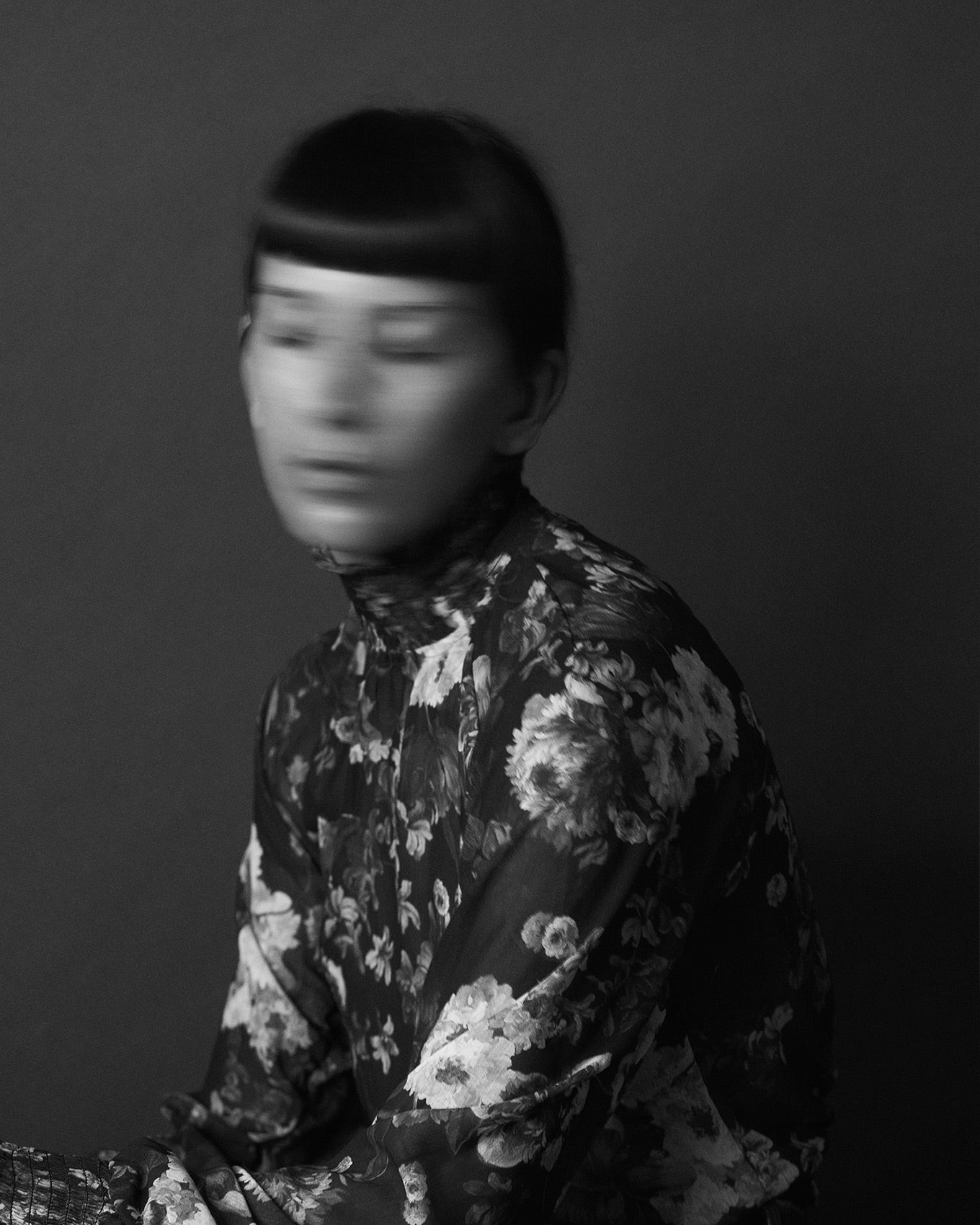 Portrait of photographer Gabriela Silveira in black and white with motion blur. Gabriela sits with her eyes closed with her arms folded wearing a floral top.