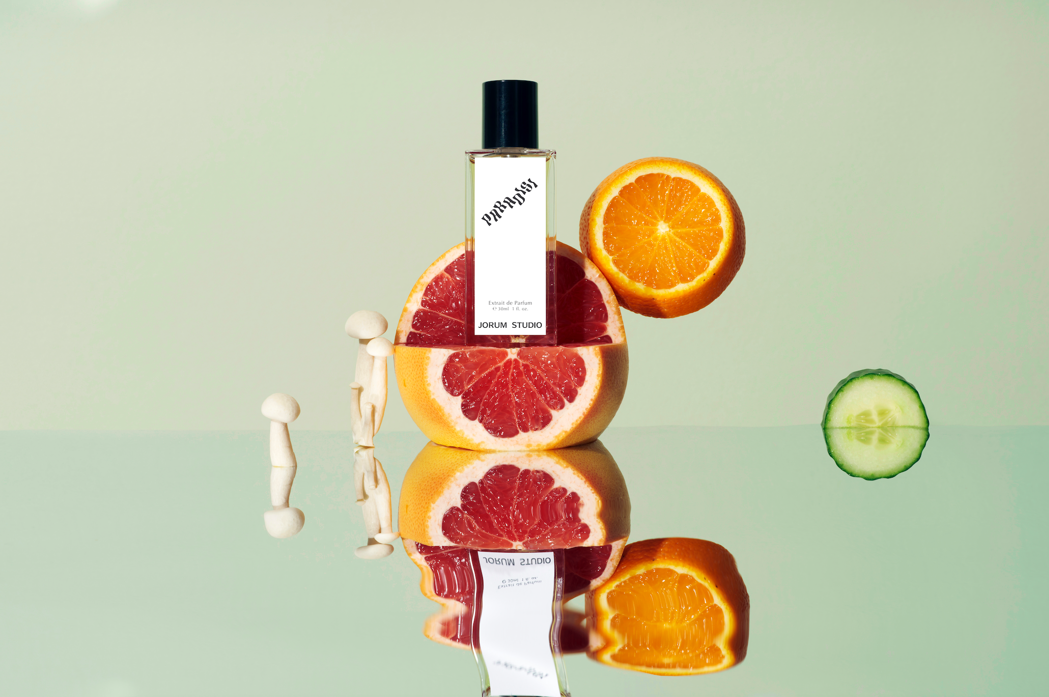 Bottle of Paradisi perfume by Jorum Studio sitting on a cut grapefruit with cucumber, mushroom and oranges