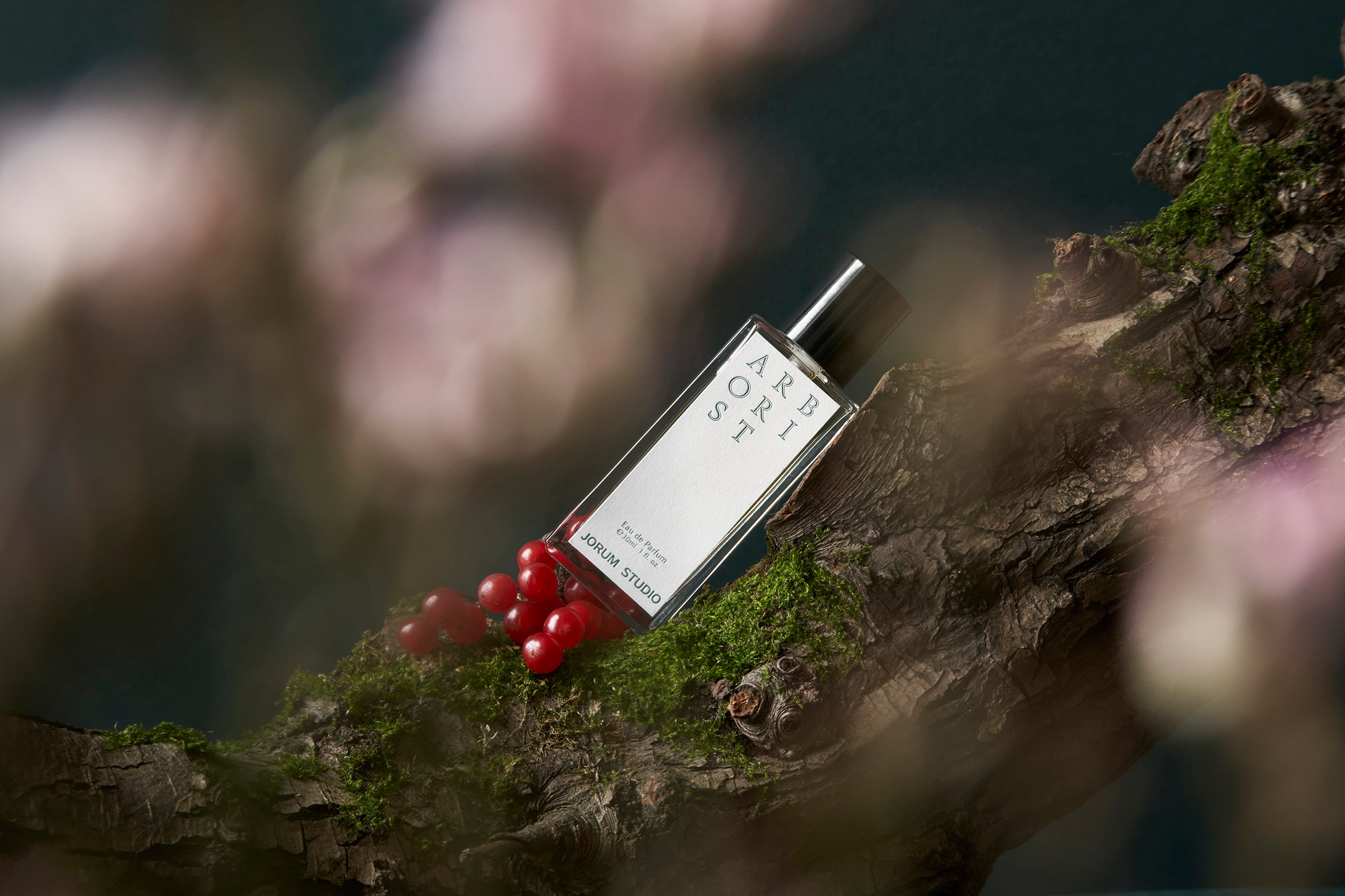 Bottle of Arborist fragrance leaning on a mossy tree branch with forest fruits and flora