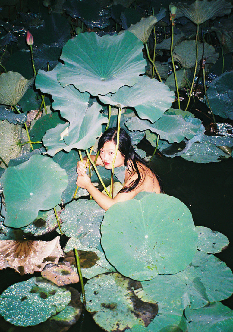Photograph of woman in pond amongst giant leaves by Ren Hang