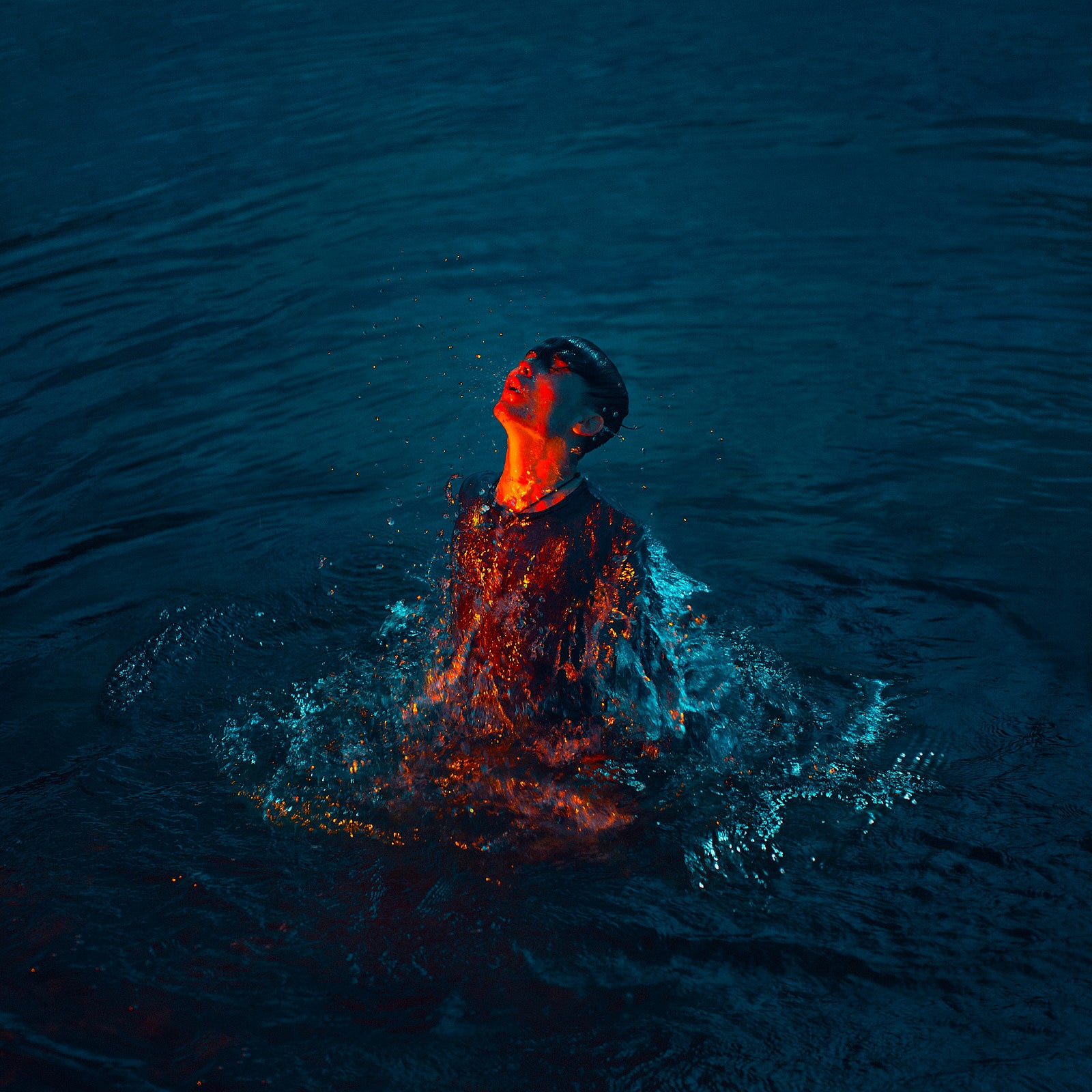 Photograph of man rising out of water with orange light on face by Adrian Wojtas