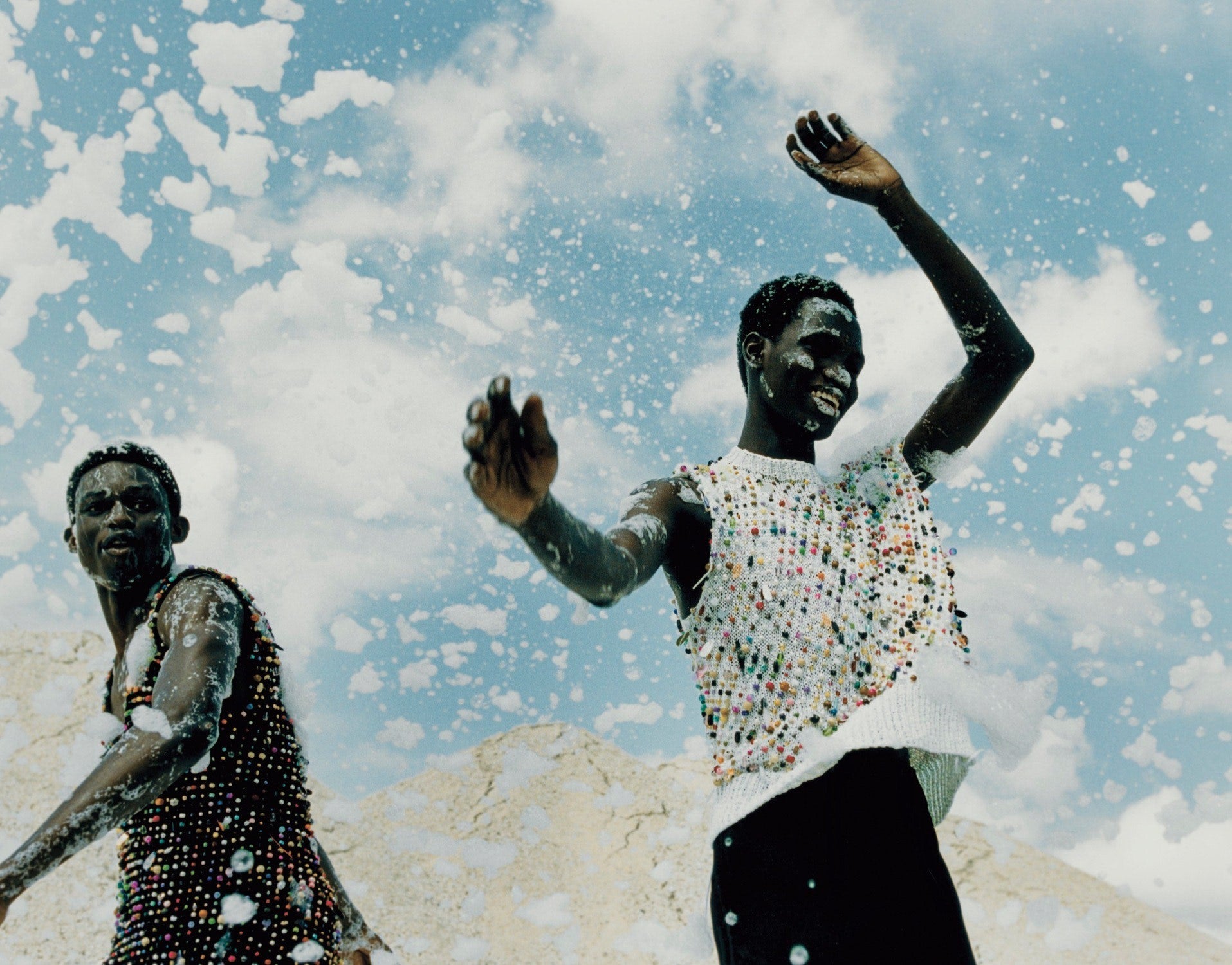 Two male models jumping and smiling with clouds of foam in the air against a blue sky by Jack Davison