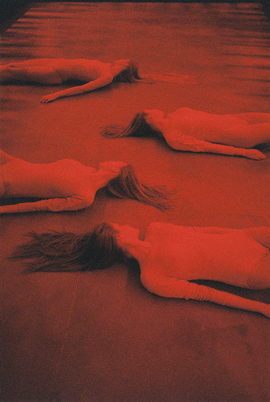 red-toned image of four people lying on the ground by Michal Pudelka